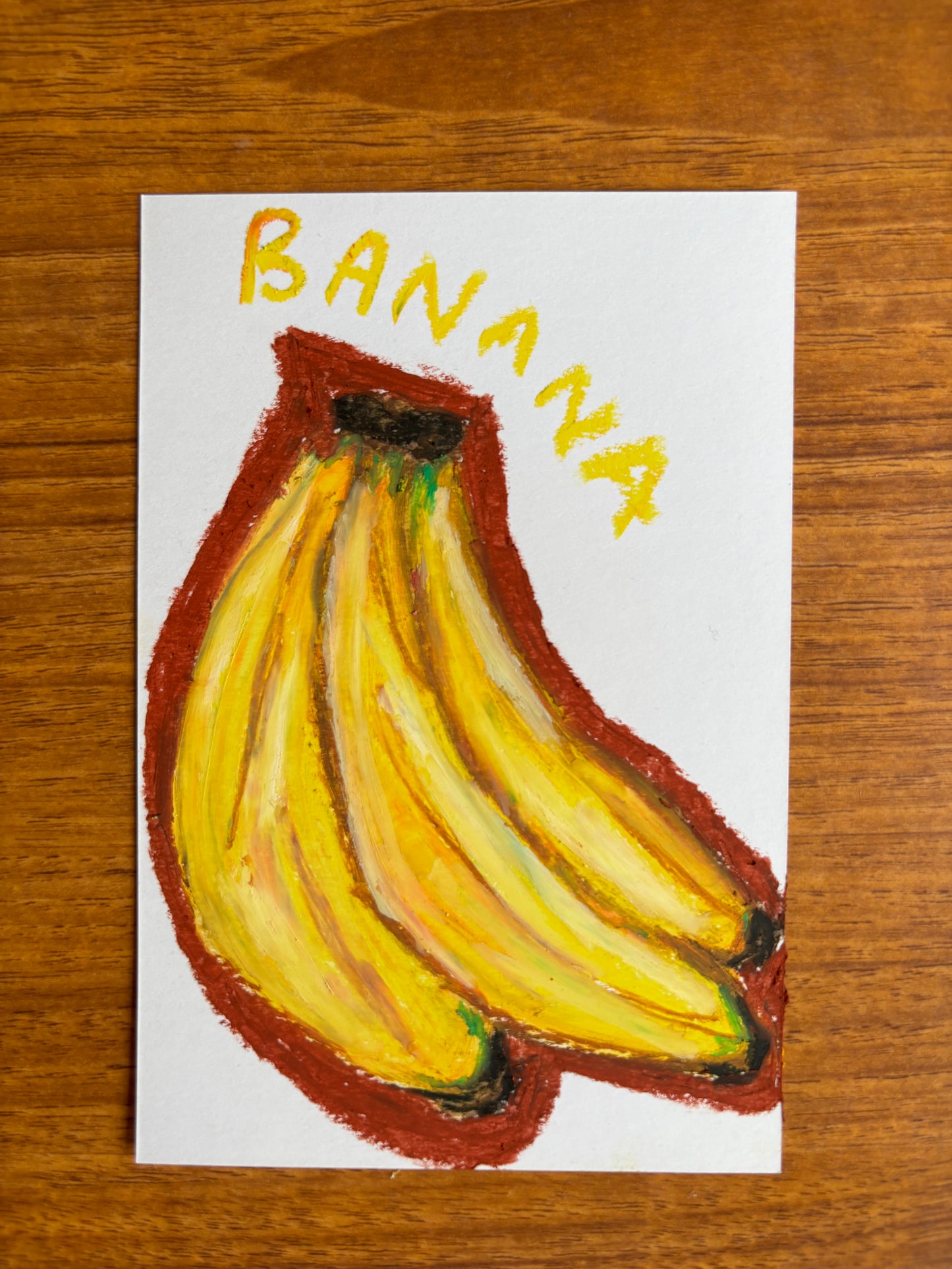 Bunch of bananas with a burnt orange outline with the text Banana on a piece of card